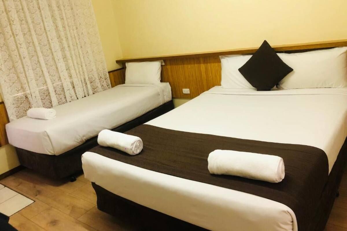 A hotel room with two beds, one larger and one smaller, both with white linens and pillows.