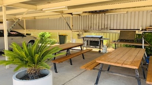 A covered outdoor area with a barbecue grill, picnic tables, and a potted plant. - Angel's Rest Motel (Moree)
