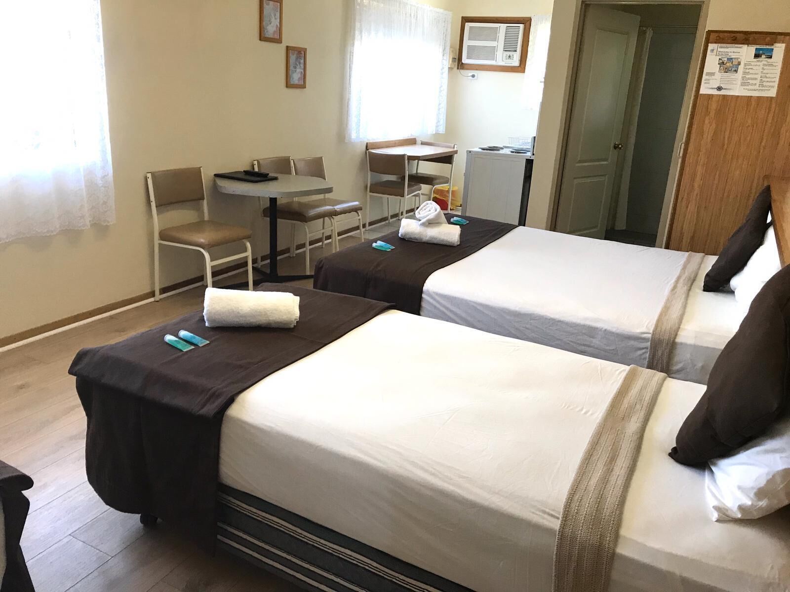 A hotel room with two beds, a desk, a chair, and a small kitchenette.