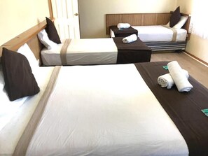 A hotel room with three beds arranged in a row, each with a headboard and pillows.
