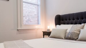 Una cama bien tendida con un cabecero oscuro, una lámpara de noche y una mesita de noche con lámpara.