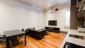 Una cocina moderna con horno empotrado, un comedor con mesa y sillas negras, y un televisor de pantalla plana montado en la pared.