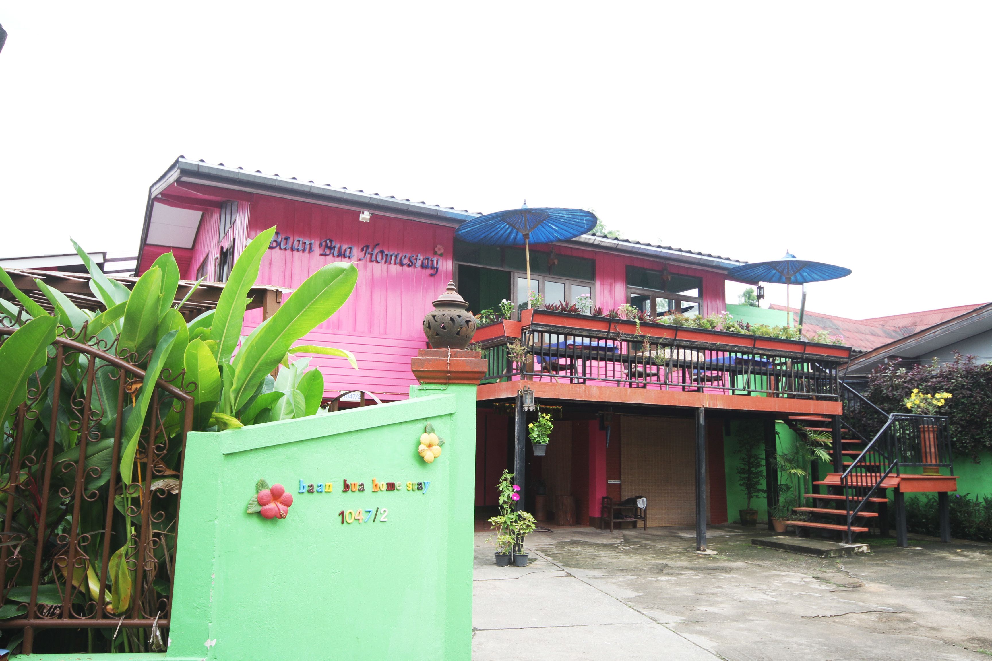A two-story building with a balcony, a staircase, and a green gate with a flower decoration.
