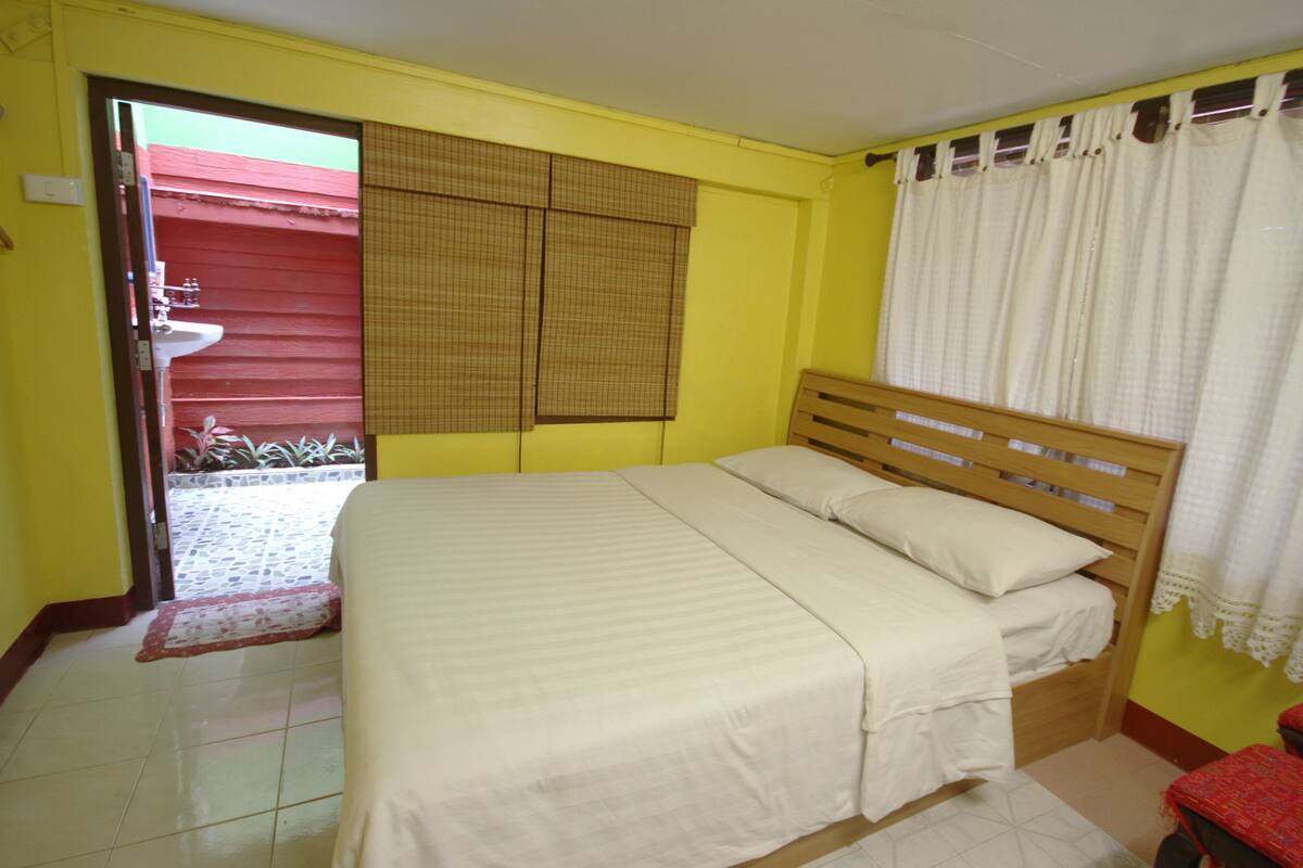 A bedroom with a bed, a window with curtains, a door leading to a balcony, and a red wall.