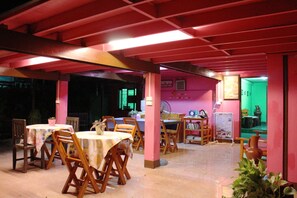 An indoor dining area with wooden tables and chairs, a pink ceiling, and a green wall in the background. - Baan Bua Homestay - Hostel (Chiang Rai)