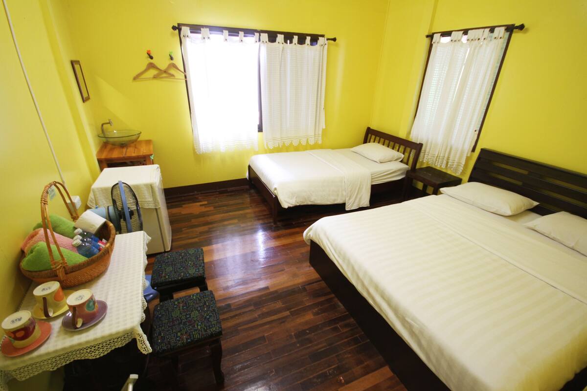 A room with two beds, a small table with a basket, and a bench.