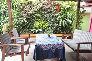 A patio area with a table covered in a blue tablecloth, surrounded by wooden chairs with striped cushions. - Baan Bua Homestay - Hostel (Chiang Rai)
