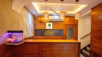 A reception desk with a wooden finish, a digital clock, and a sign for Hotel Anam International.