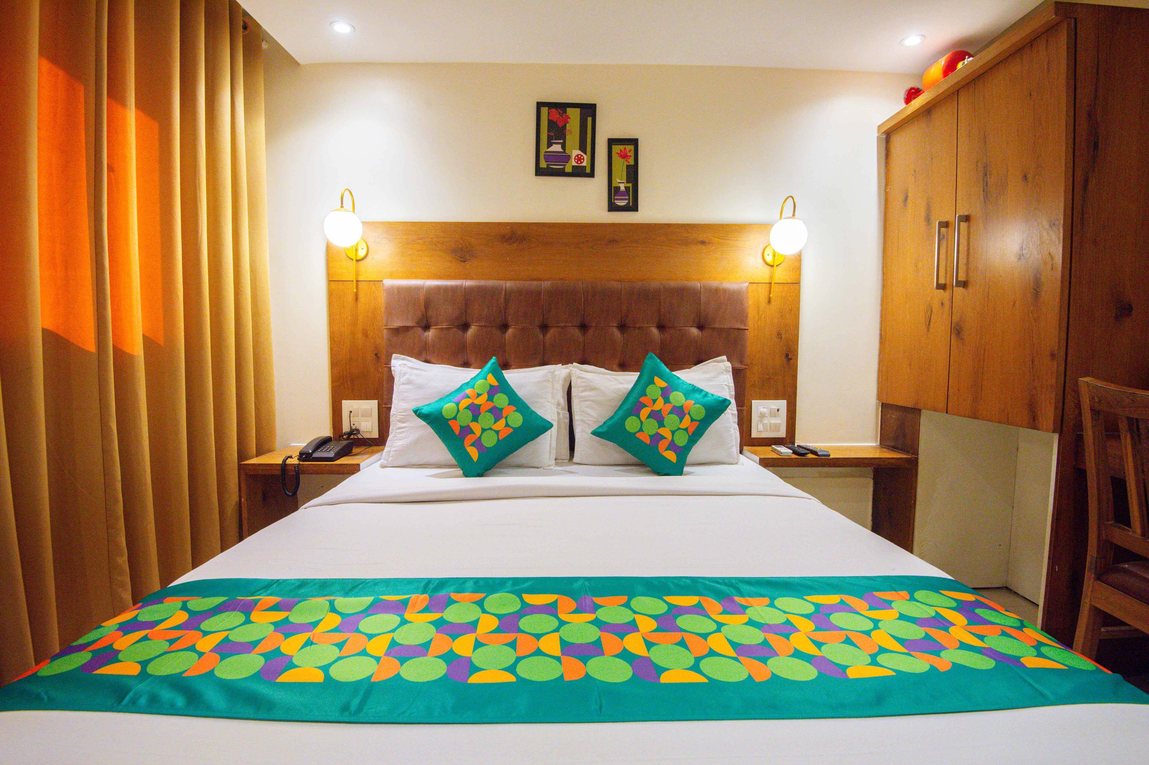 A hotel room with a large bed, two bedside tables, a wooden headboard, and a colorful bedspread.