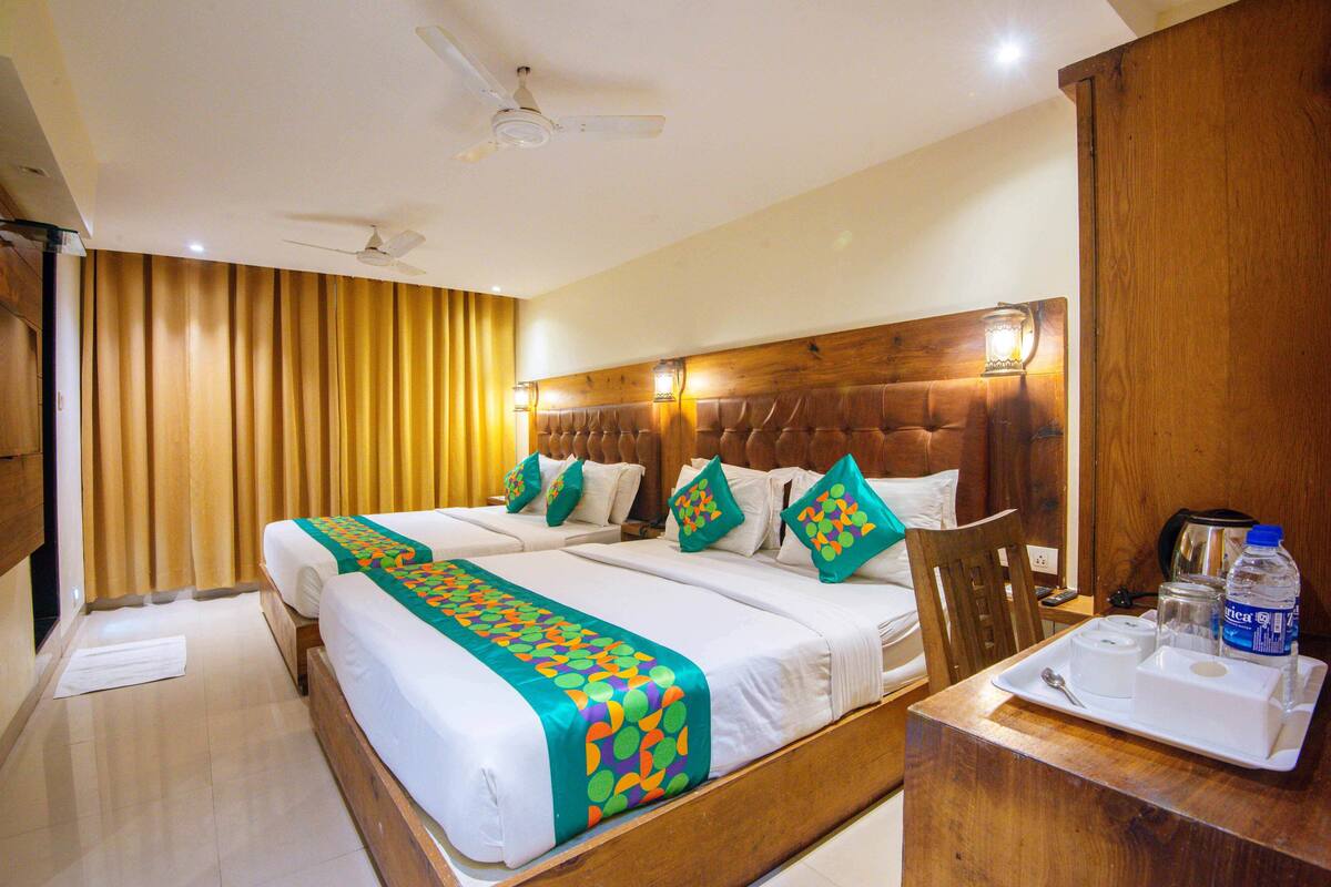 A hotel room with two beds, wooden headboard, a wooden desk with a tray, a ceiling fan, and a window with curtains.
