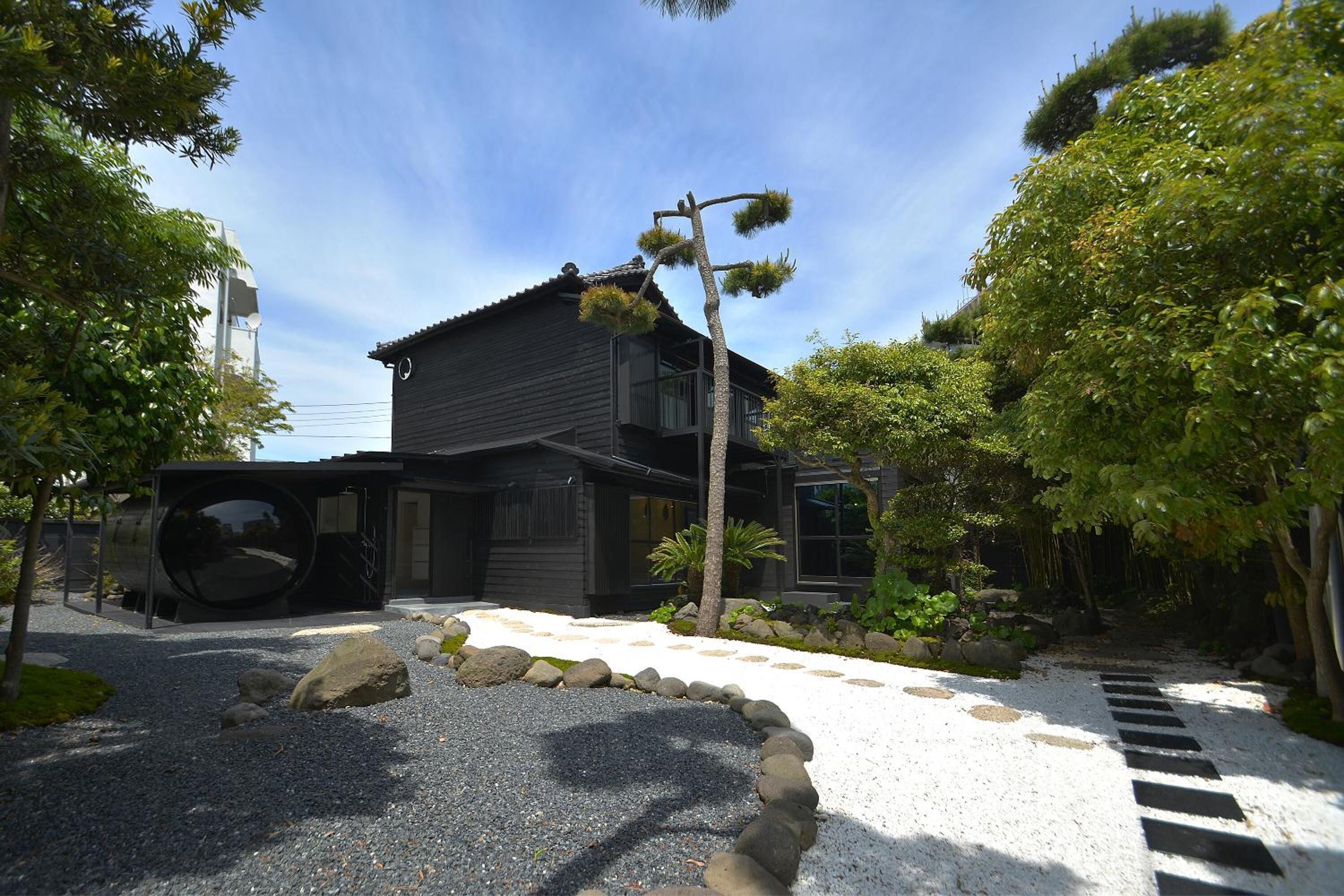A traditional Japanese house with a dark exterior, surrounded by a gravel path and a stone border.
