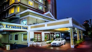 A hotel with a prominent sign reading "Krishna Inn" and a modern building with a red-lit tower. - Krishna Inn (Chavakkad)