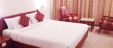 A hotel room with a large bed, two pillows, a wooden nightstand, a small table, and a chair.