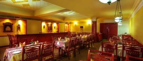 Un restaurante con mesas y sillas de madera, manteles a cuadros rojos y blancos, y lámparas colgantes.