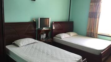 A room with two single beds, a desk with a computer, a wall-mounted lamp, and a window with curtains.