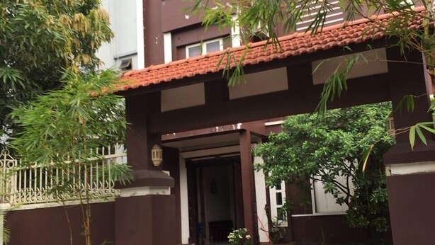 A building with a red-tiled roof, a gated entrance, and a small garden area with potted plants. - Nha Nghi Tham Quyen (Mong Duong)