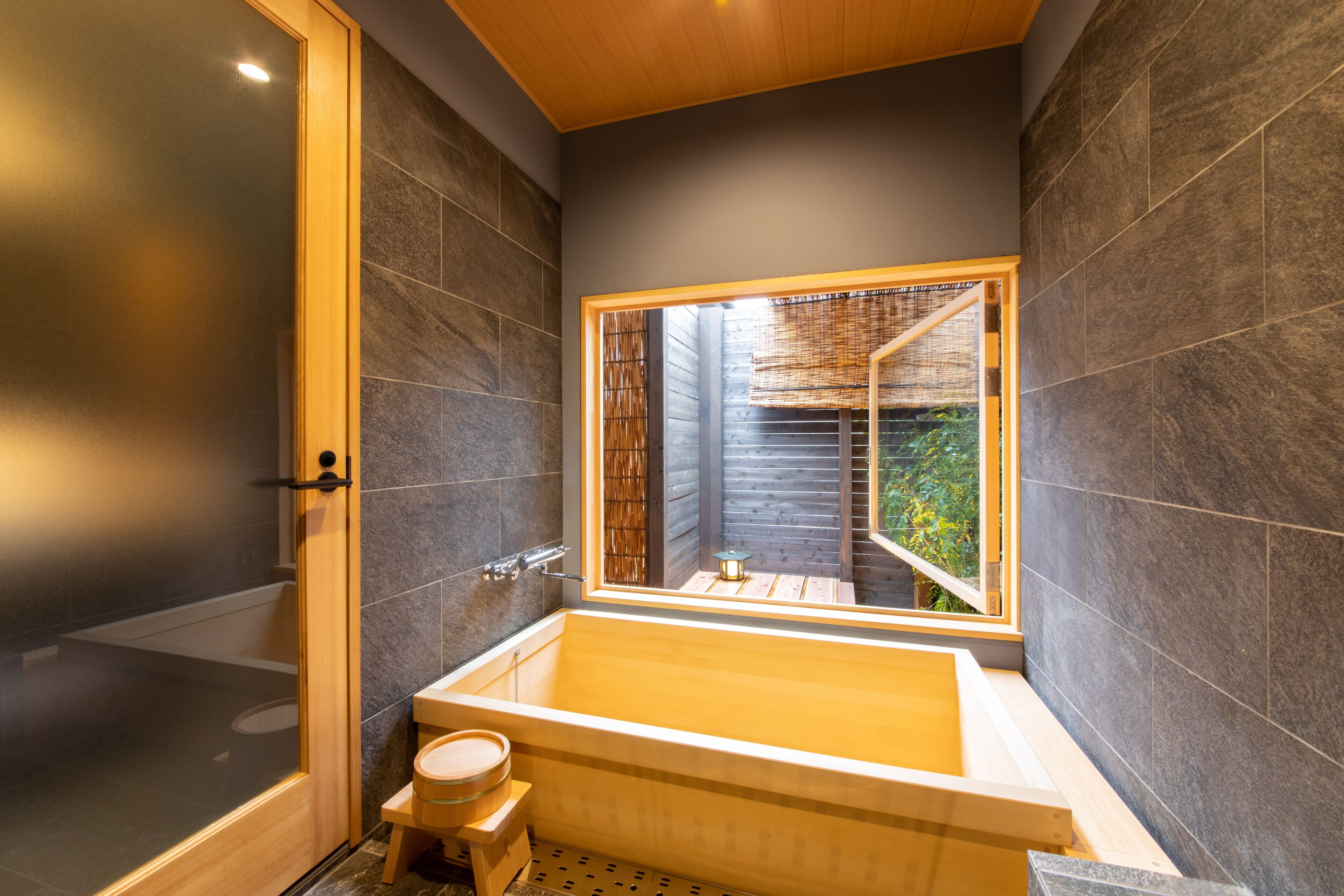 Un baño moderno con una bañera grande, un taburete de madera y una ventana con vistas al exterior.