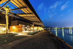 A waterfront hotel with a covered outdoor seating area, a palm tree, and a view of the water. - Nihon Iro (Shizuoka)