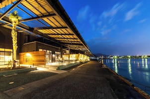 A waterfront hotel with a covered outdoor seating area, a palm tree, and a view of the water.