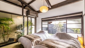 A modern bedroom with a large bed, wooden beams, large windows, and indoor plants. - Nihon Iro (Shizuoka)
