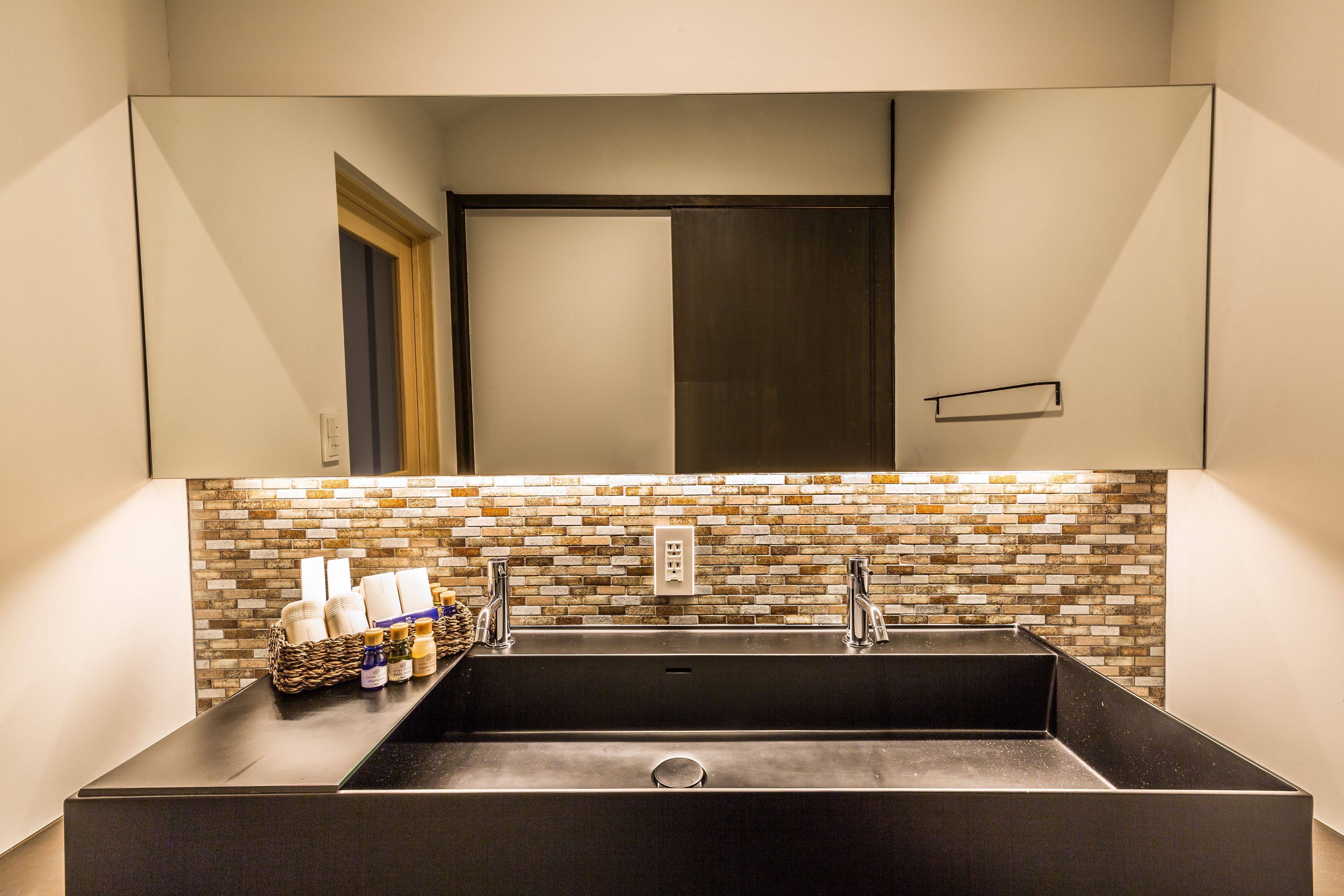 Un baño moderno con un espejo grande, un lavabo negro y un respuesto de mosaicos.
