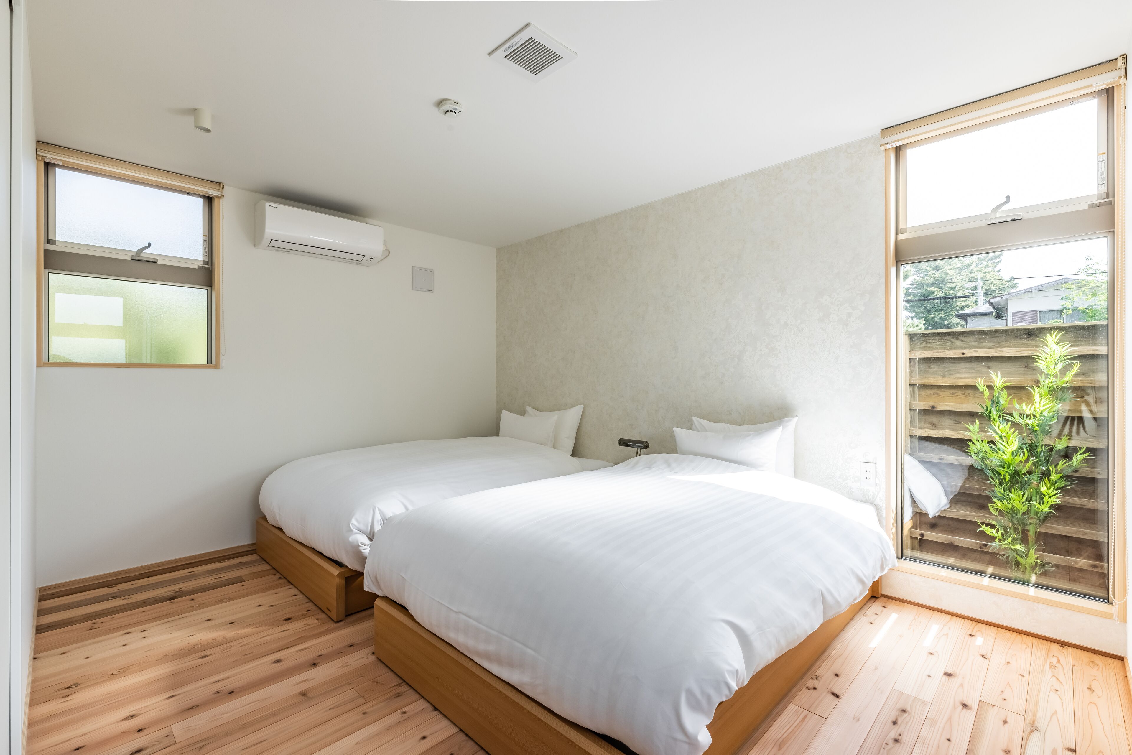 Een slaapkamer met twee bedden, houten vloeren, een raam met zonwering en een airconditioning.