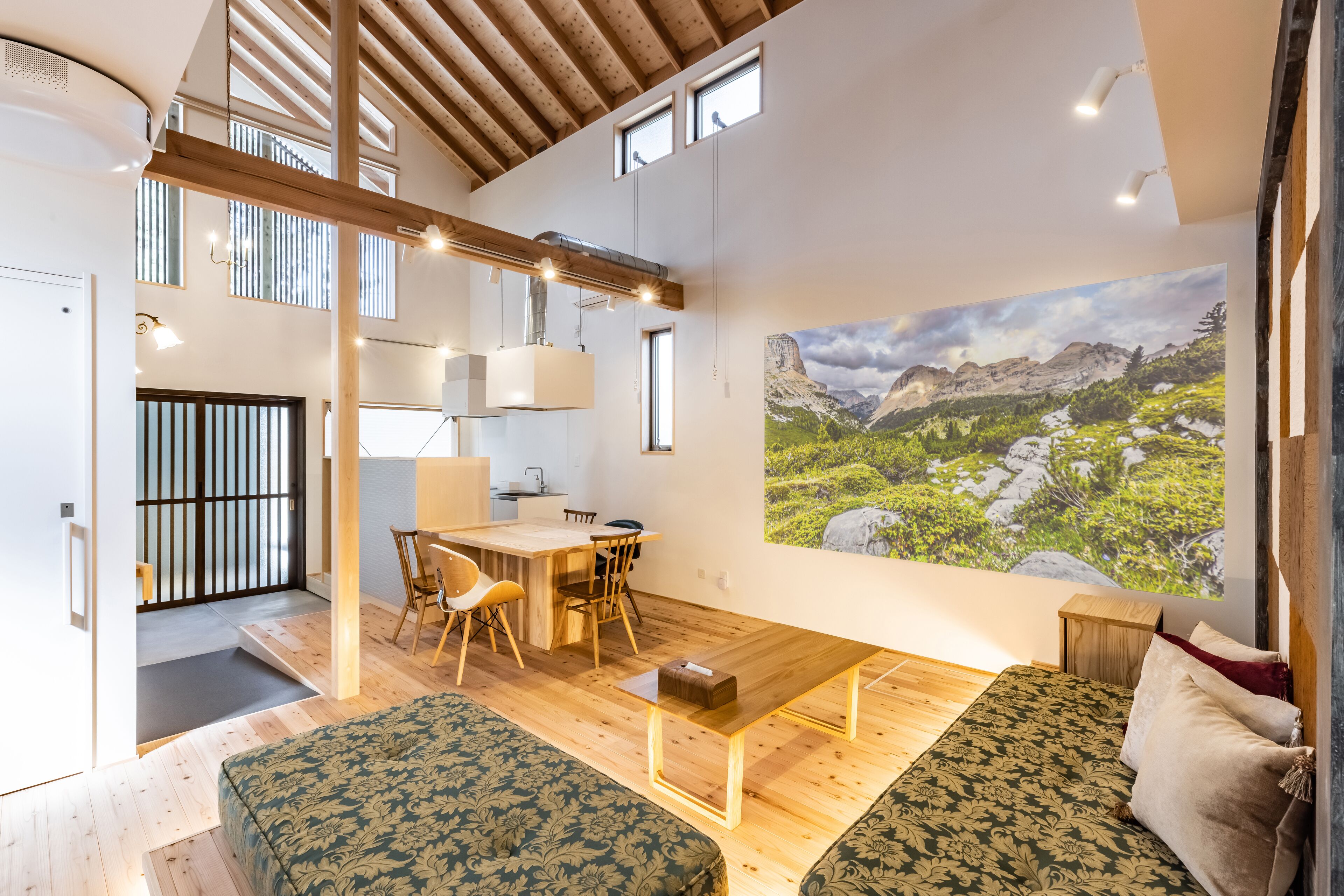 A spacious living area with a wooden ceiling, a large painting of a mountainous landscape, a dining table with chairs, and a sofa.