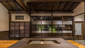 A modern interior with a wooden floor, a central table, and sliding glass doors leading to a garden. - Nihon Iro (Shizuoka)