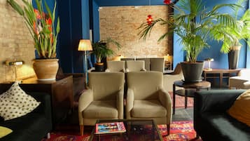 A modern living room with a brick wall, two beige armchairs, a coffee table with magazines, and potted plants.