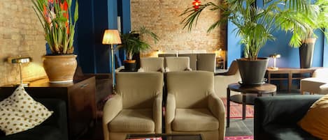 Ein modernes Wohnzimmer mit einer Ziegelwand, zwei beigen Sesseln, einem Couchtisch mit Zeitschriften und Blumentöpfen.