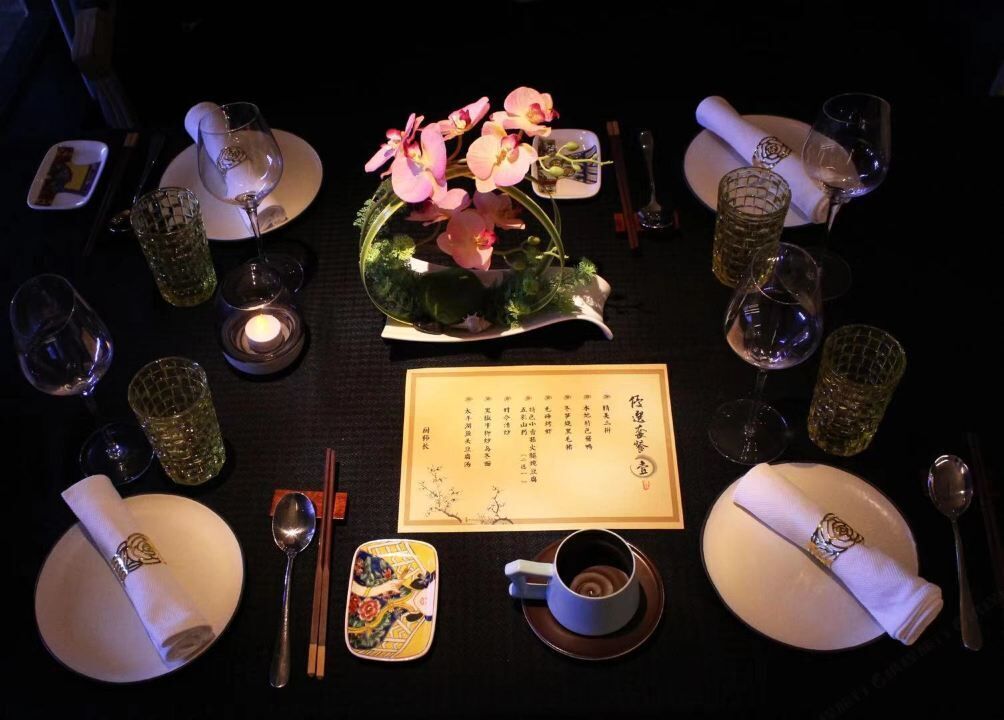 Une table dressée pour un repas, avec un menu, des baguettes, une tasse et un arrangement floral décoratif composé d’une orchidée.