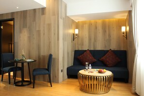 Ein modernes Zimmer mit einer Holzvertäfelung, einem dunkelblauen Sofa mit zwei roten Kissen, einem runden Holztisch, zwei blauen Stühlen und einem kleinen runden Tisch mit einer Vase und Büchern.