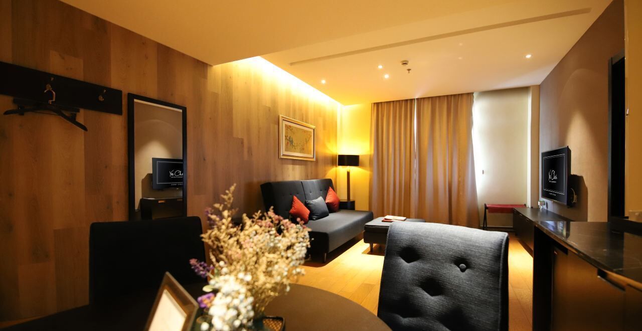 Moderni hotellihuone, jossa on puinen seinä, punaisilla tyynyillä varustettu sohva, ruokapöytä ja televisio.