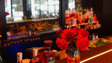 A bar area with bottles of liquor, a vase with red roses, and a reflection of the interior.