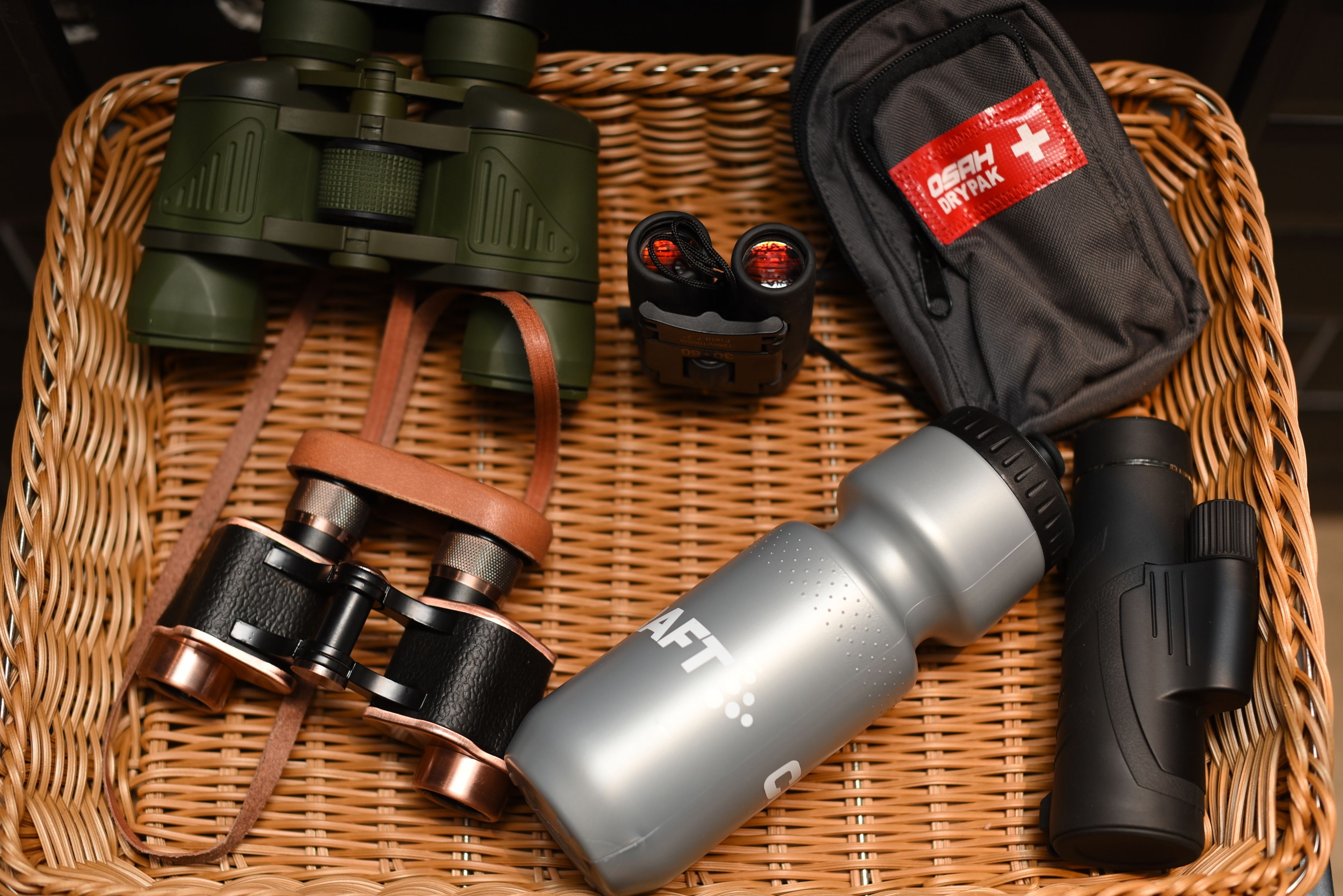 Un panier en osier contenant une paire de jumelles, une lampe de poche, une bouteille d’eau et une trousse de premiers secours.