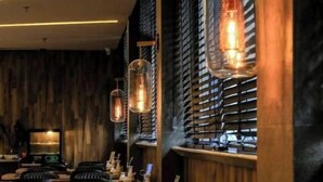 L’intérieur d’un restaurant présente des murs en bois, des stores métalliques et des lampes suspendues. Les tables sont dressées avec des couverts et des serviettes.