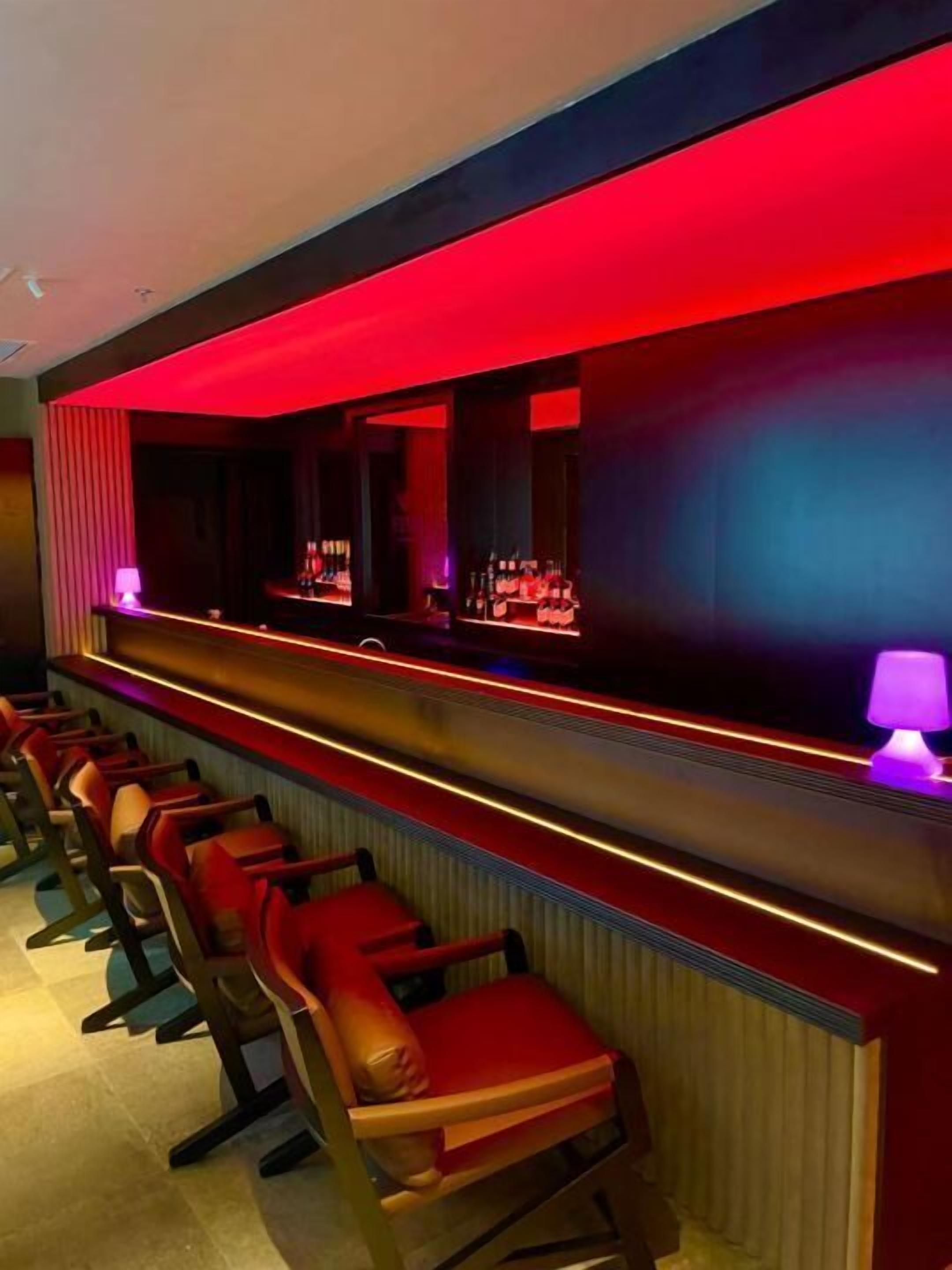 Eine Bar mit roter Beleuchtung, einer Theke und mehreren Sesseln.