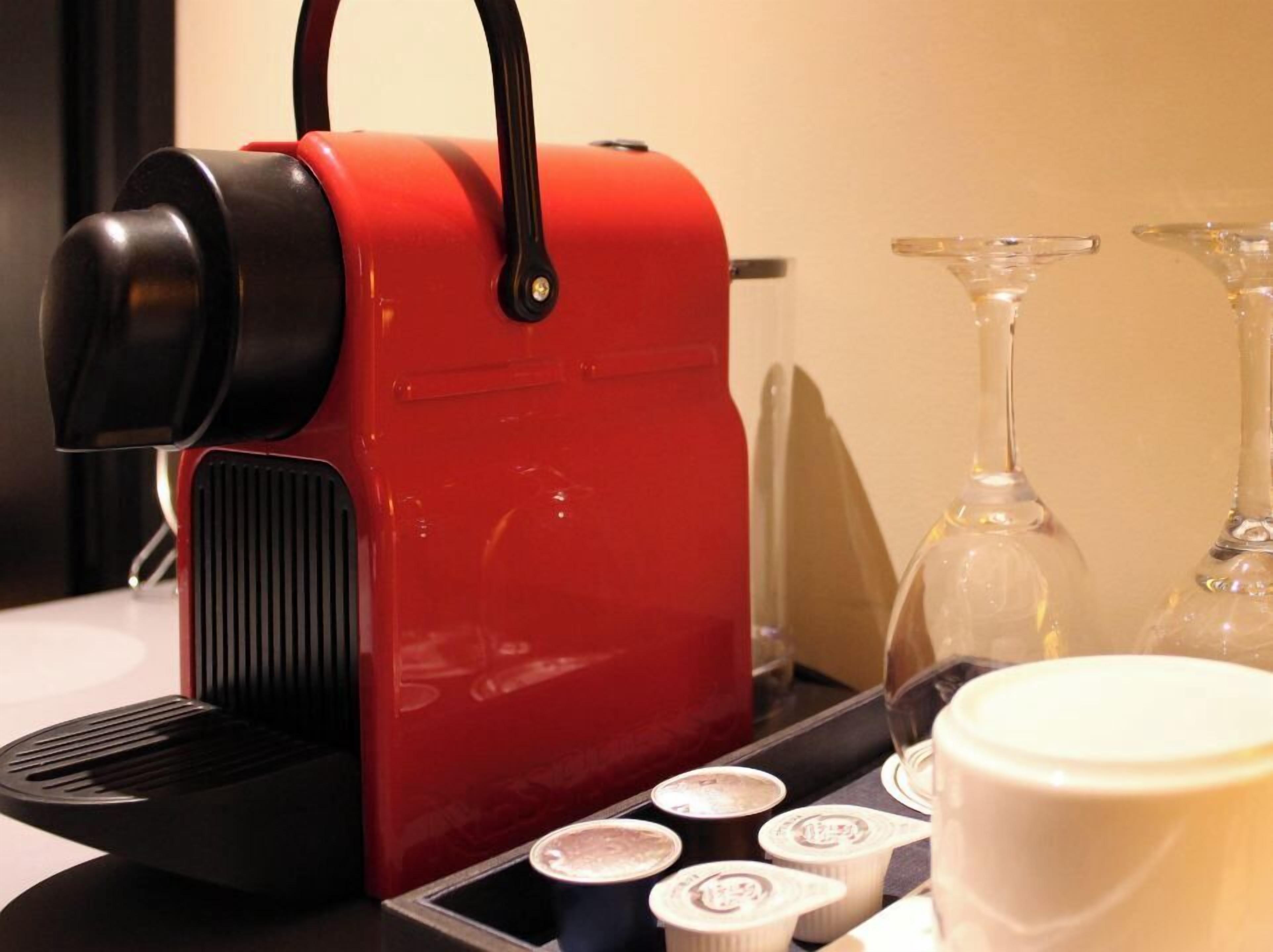 A red espresso machine with a black handle, a coffee maker, and several cups of coffee on a tray.