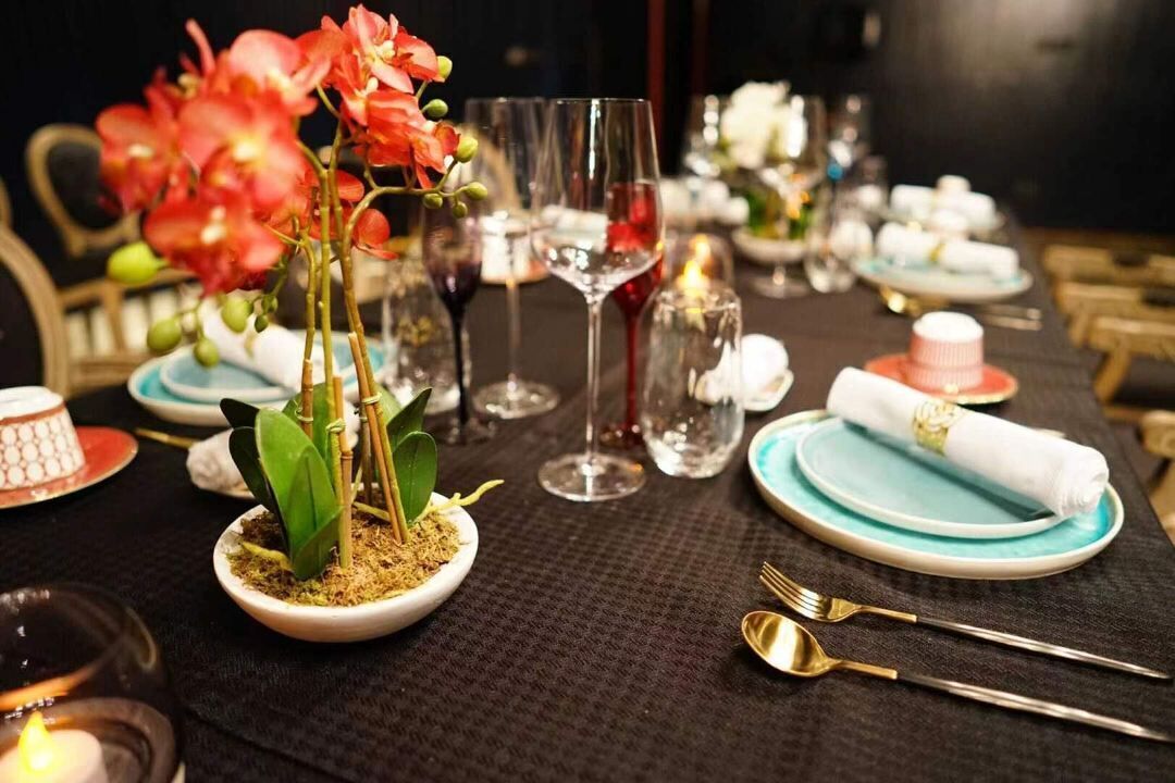 A table set with plates, glasses, and cutlery, with a small plant and a candle.