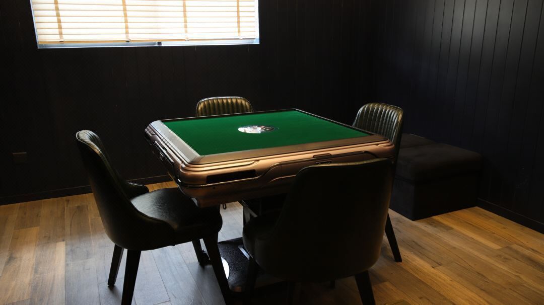 Una mesa de billar con cuatro sillas, una ventana con persianas y suelo de madera.