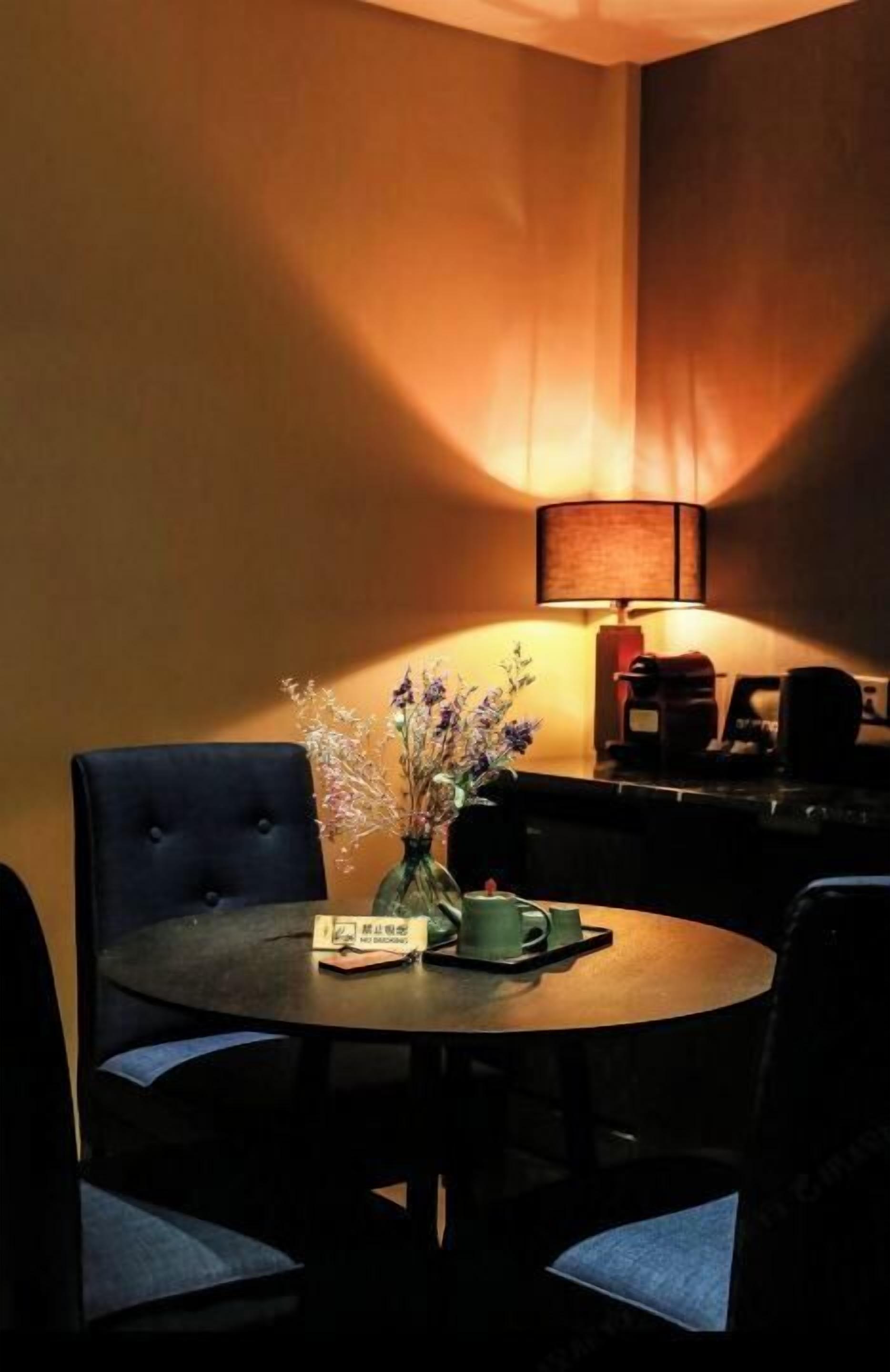 A dining area with a round table, two chairs, a vase with flowers, a book, and a coffee machine in the background.