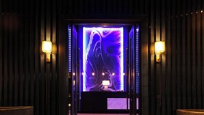 Une pièce avec un mur éclairé de lumière violette et une petite table sur laquelle se trouve une lampe.