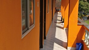 A corridor with orange walls and tiled flooring, leading to a covered area with a blue trash bin. - Villa Mer (Baga)