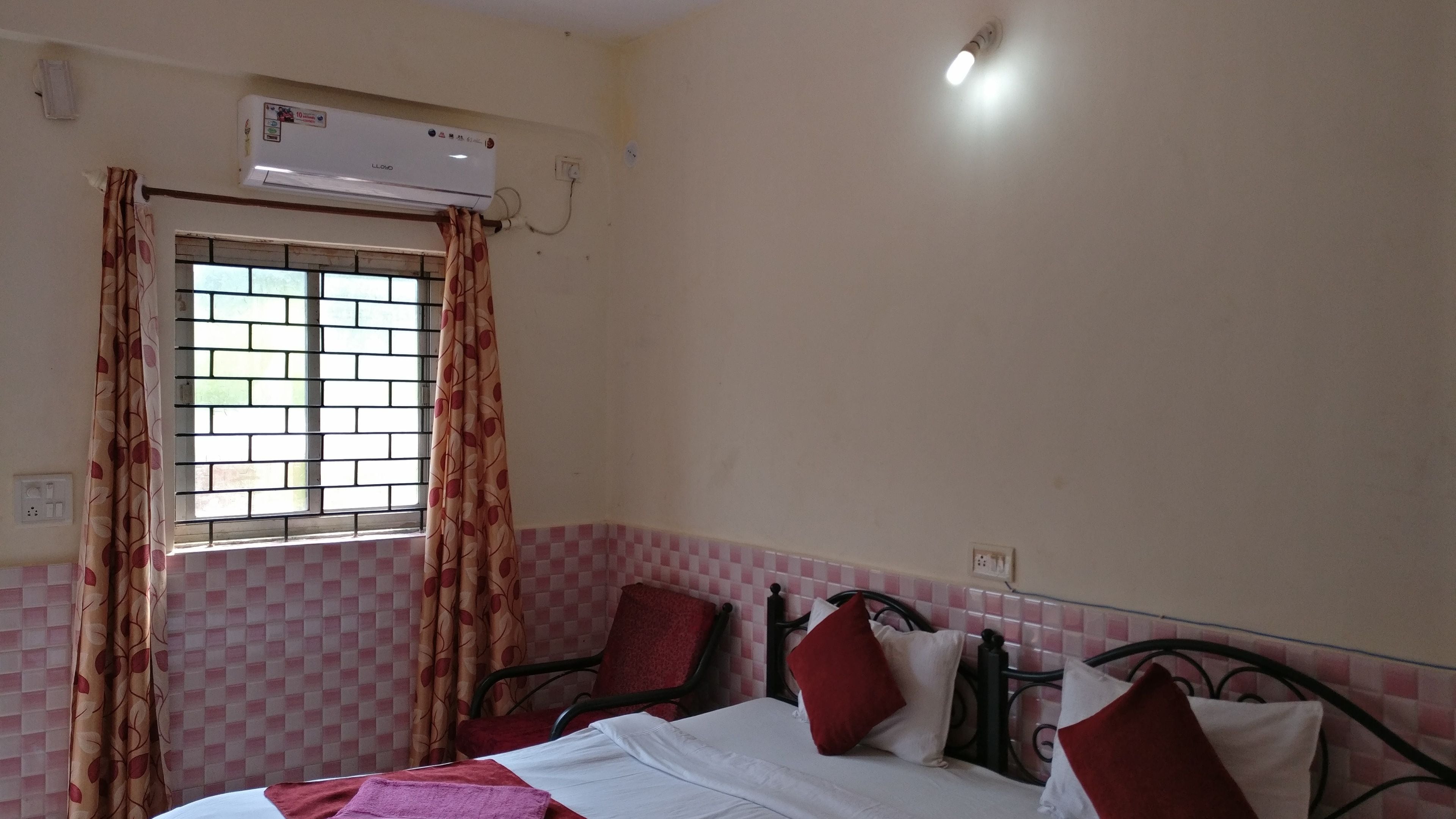 A bedroom with a bed, a window with curtains, a wall-mounted air conditioner, and a checkered wall pattern.