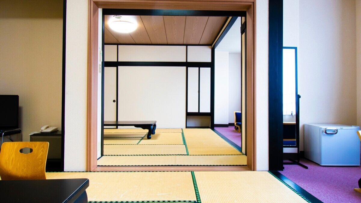Une pièce de style japonais traditionnel, avec un sol recouvert de tatamis, un futon servant de lit, une télévision et un petit réfrigérateur.