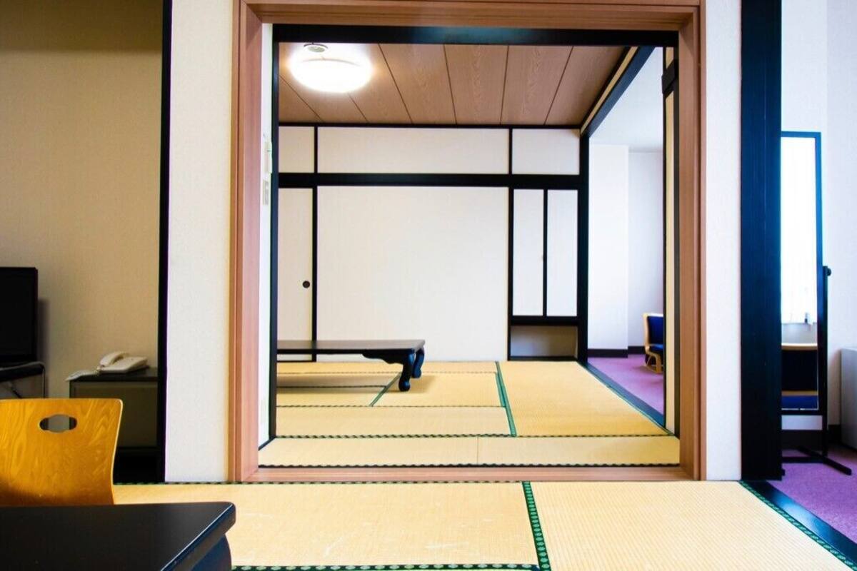 Une pièce de style japonais traditionnel, avec un sol recouvert de tatamis, un futon servant de lit, une télévision et un petit réfrigérateur.