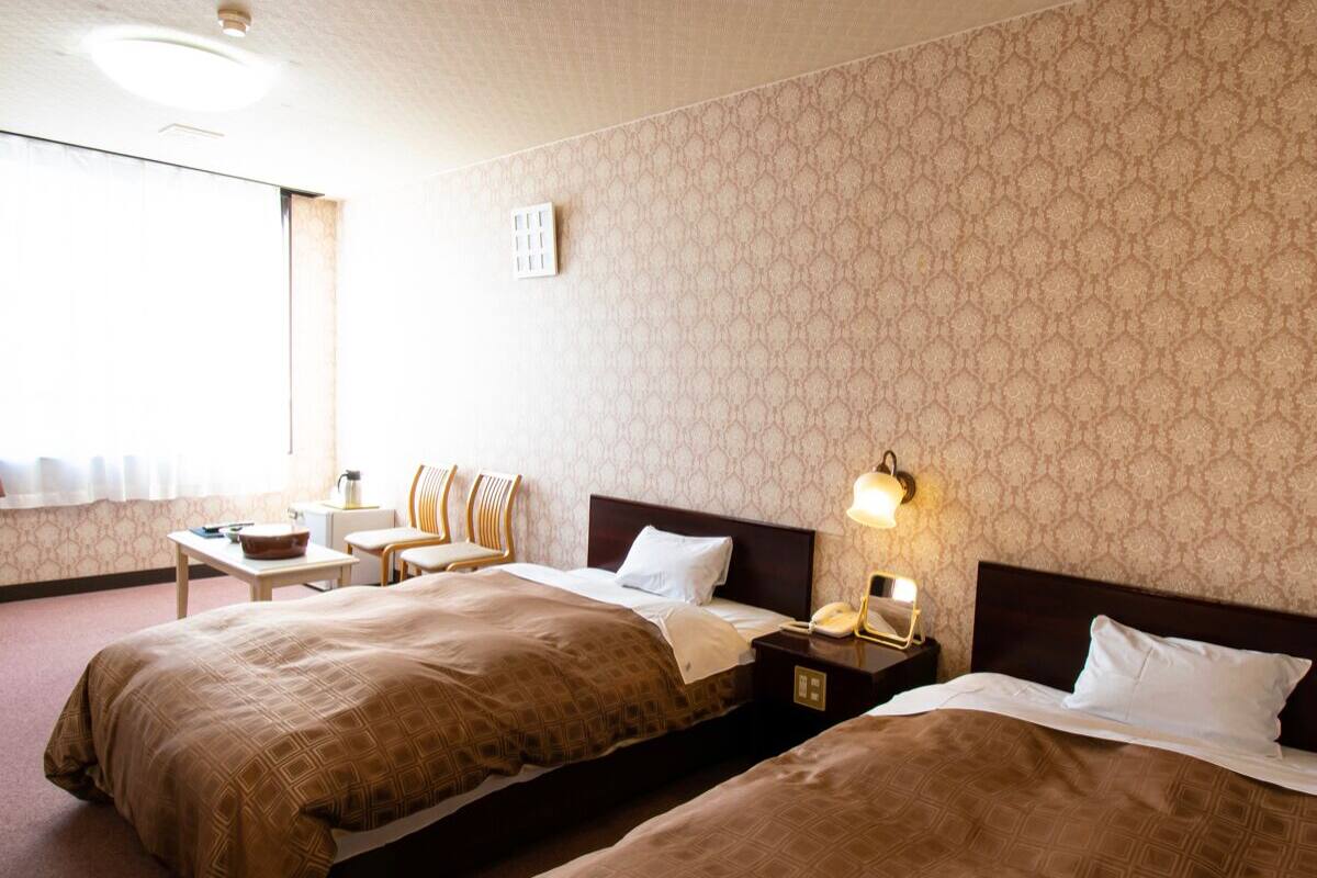 Ein Hotelzimmer mit zwei Betten, einem Schreibtisch, einem Stuhl und einem Nachttisch mit Lampe.