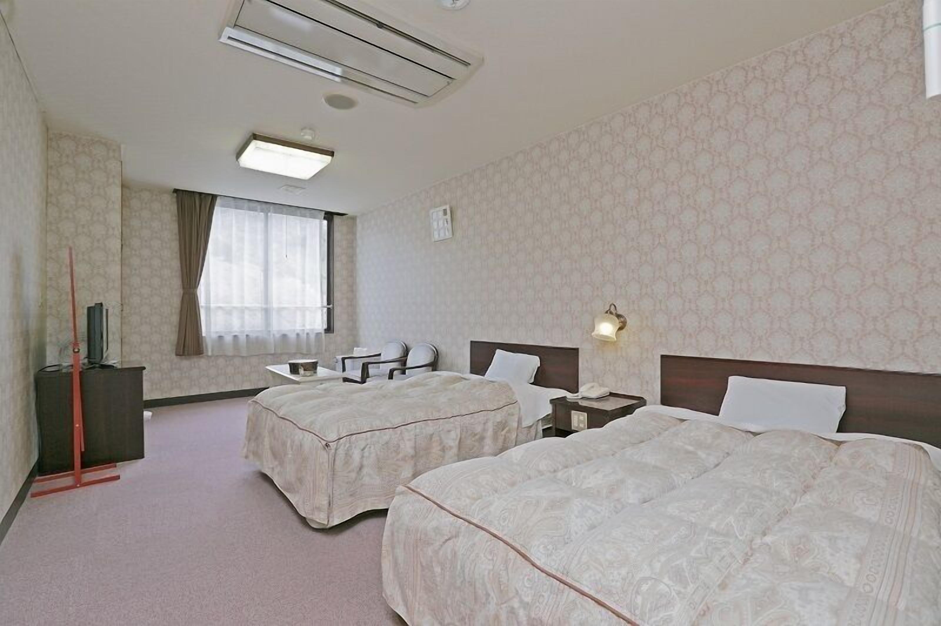 Een hotelkamer met twee bedden, een bureau, een stoel, een televisie en een raam met gordijnen.