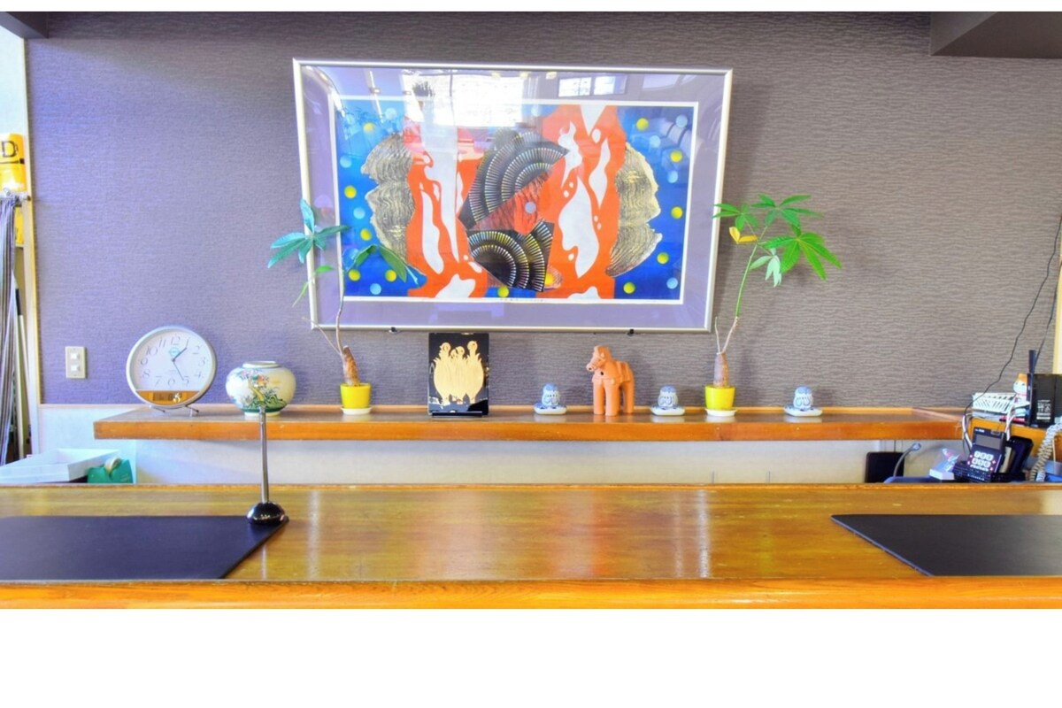 A reception desk with a framed artwork above it, a clock, and several potted plants.