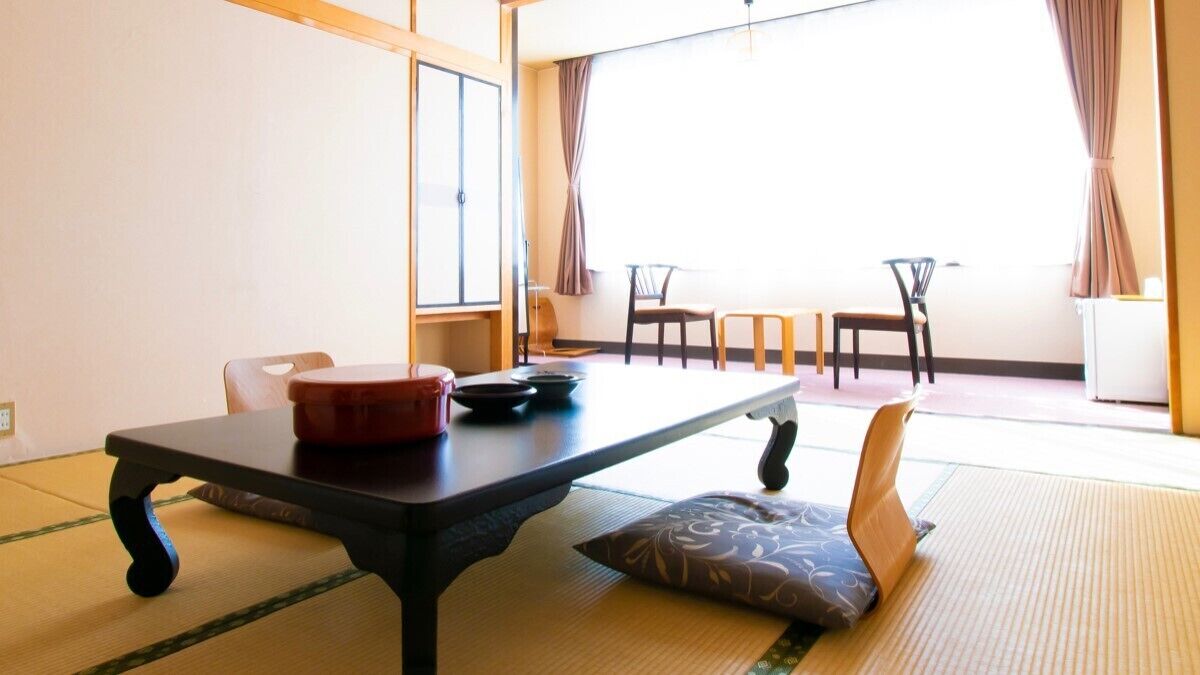 Une pièce de style japonais traditionnel, avec un sol recouvert de tatamis, une petite table et un récipient rouge, ainsi que deux chaises.